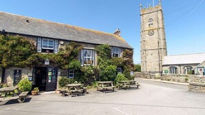 Un bâtiment traditionnel en pierre, doté d’un clocher, un pub avec une terrasse et un mur en pierre.