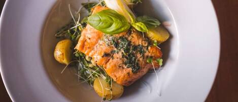 A white plate with a piece of salmon, potatoes, and greens.