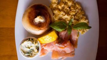 Un plato con un bagel, huevos revueltos, salmón ahumado, un cuenco pequeño de queso crema y una hoja de albahaca.