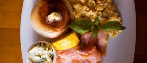 Un plato con un bagel, huevos revueltos, salmón ahumado, un cuenco pequeño de queso crema y una hoja de albahaca.