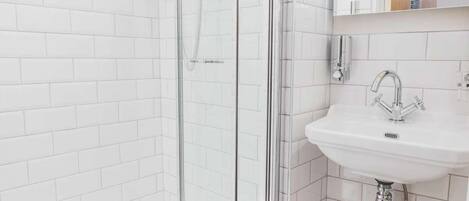 A modern bathroom with white subway tiles, a glass shower enclosure, a wooden floor, and a white sink with a mirror above it.