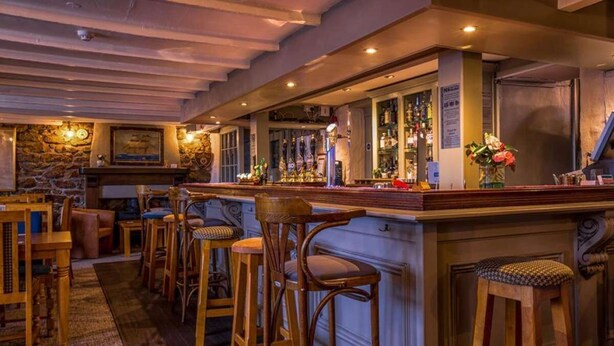 Un espace bar avec des tabourets en bois, un mur en pierre et un comptoir où sont exposées des bouteilles.