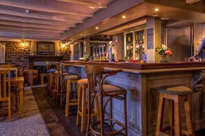 Un espace bar avec des tabourets en bois, un mur en pierre et un comptoir où sont exposées des bouteilles.
