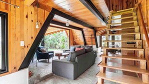 Geräumiges Loft mit großem grauen Ecksofa, einer Holztreppe und Blick auf Grünflächen.