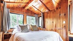 Ein Schlafzimmer in einer Holzhütte mit einem großen Bett, zwei Fenstern und einer Holzbalkendecke.