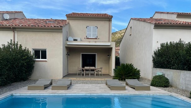 Et moderne hus med en swimmingpool, en terrasse med stole og et lille bord.