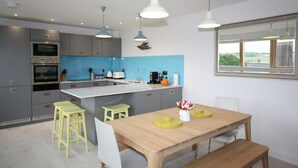 Una cocina moderna con gabinetes grises, una isla central y un comedor con una mesa de madera y taburetes amarillos.