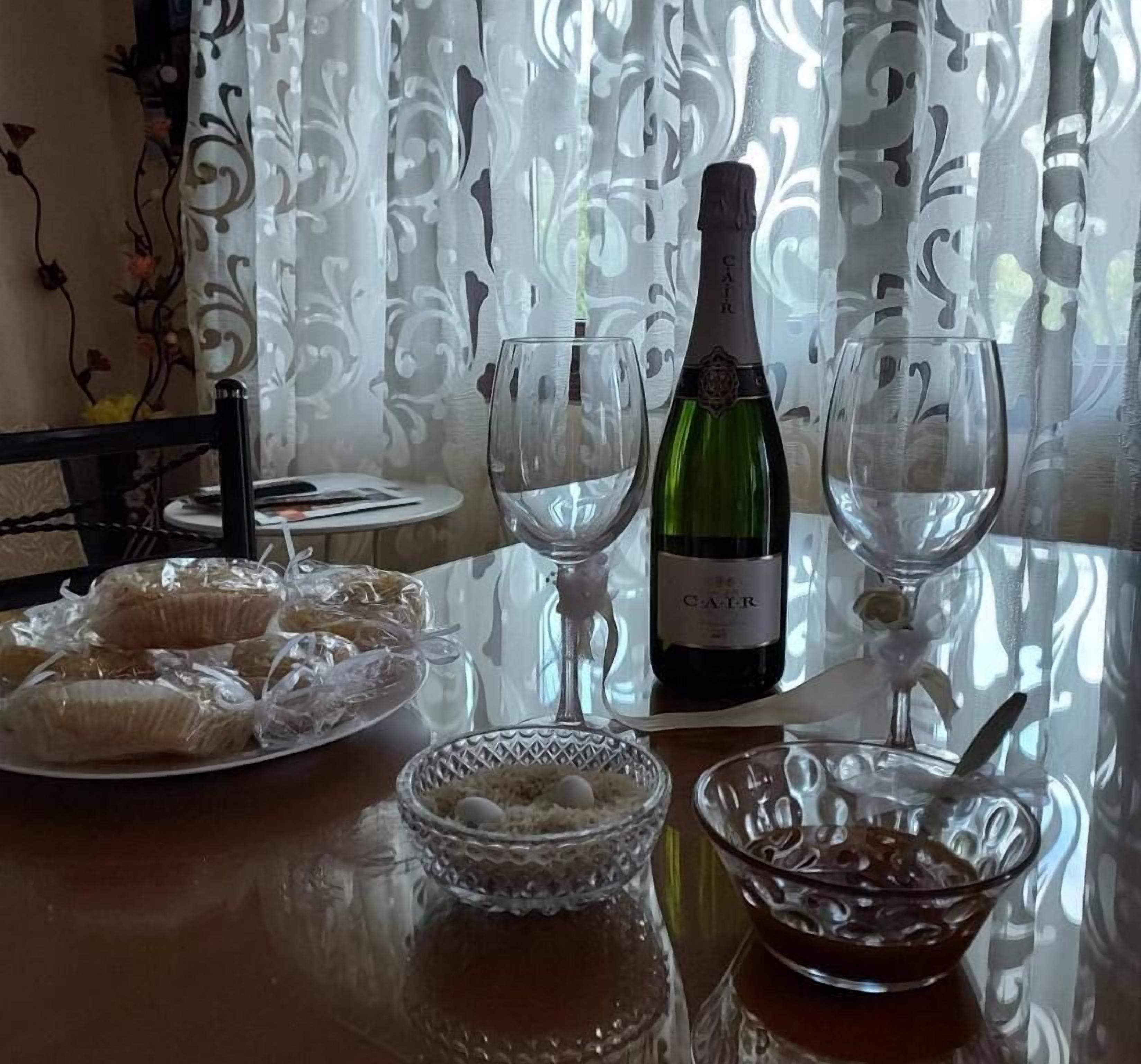 Une table à manger avec une bouteille de vin, deux verres à vin vides, une assiette avec de la nourriture et un bol avec une cuillère.