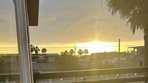 A balcony with a chair and a cushion, overlooking a residential area with palm trees and a sunset. - CASA COLONIAL PLAYAS  CHAPULTEPEC DOS CUADRAS DE LA PLAYA GRANDE PARKING ADENTRO (Colonia Playas de Chapultepec Ensenada)