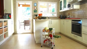 Een keuken met witte kastjes, een magnetron, een oven en een mand met fruit op het aanrecht.