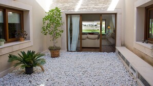 Een modern interieur met een patio, voorzien van witte kiezels, een potplant en een schuifdeur naar een zithoek met een bank en een lamp.