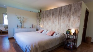 Een slaapkamer met een groot bed, een nachtkastje met een lamp, een stoel en een houten vloer.