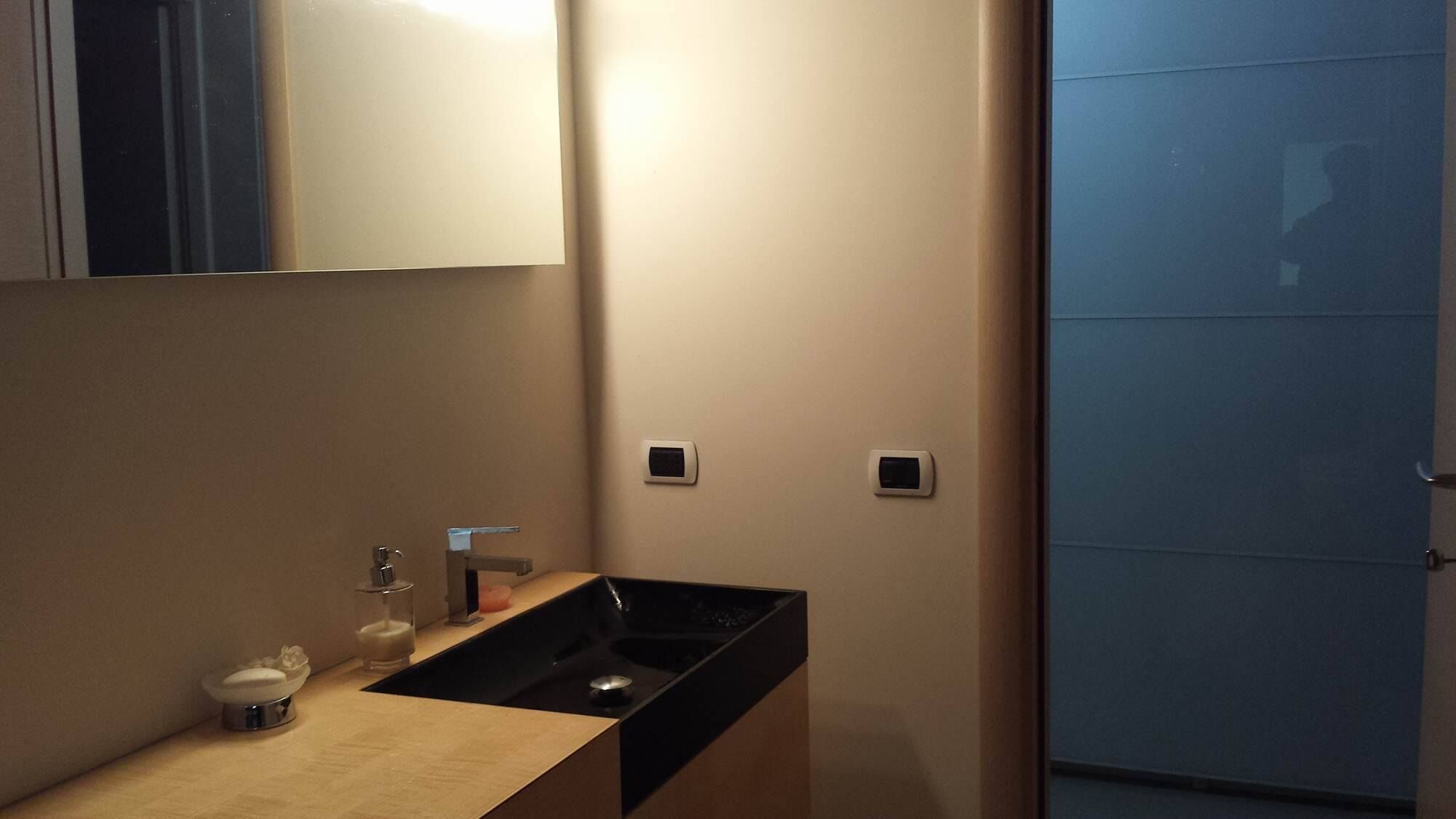 Une salle de bain moderne avec un lavabo, un miroir et deux interrupteurs muraux.
