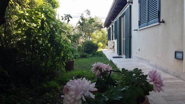 Ein Gartenweg führt zu einem Gebäude mit grünen Fensterläden und einer weißen Wand.