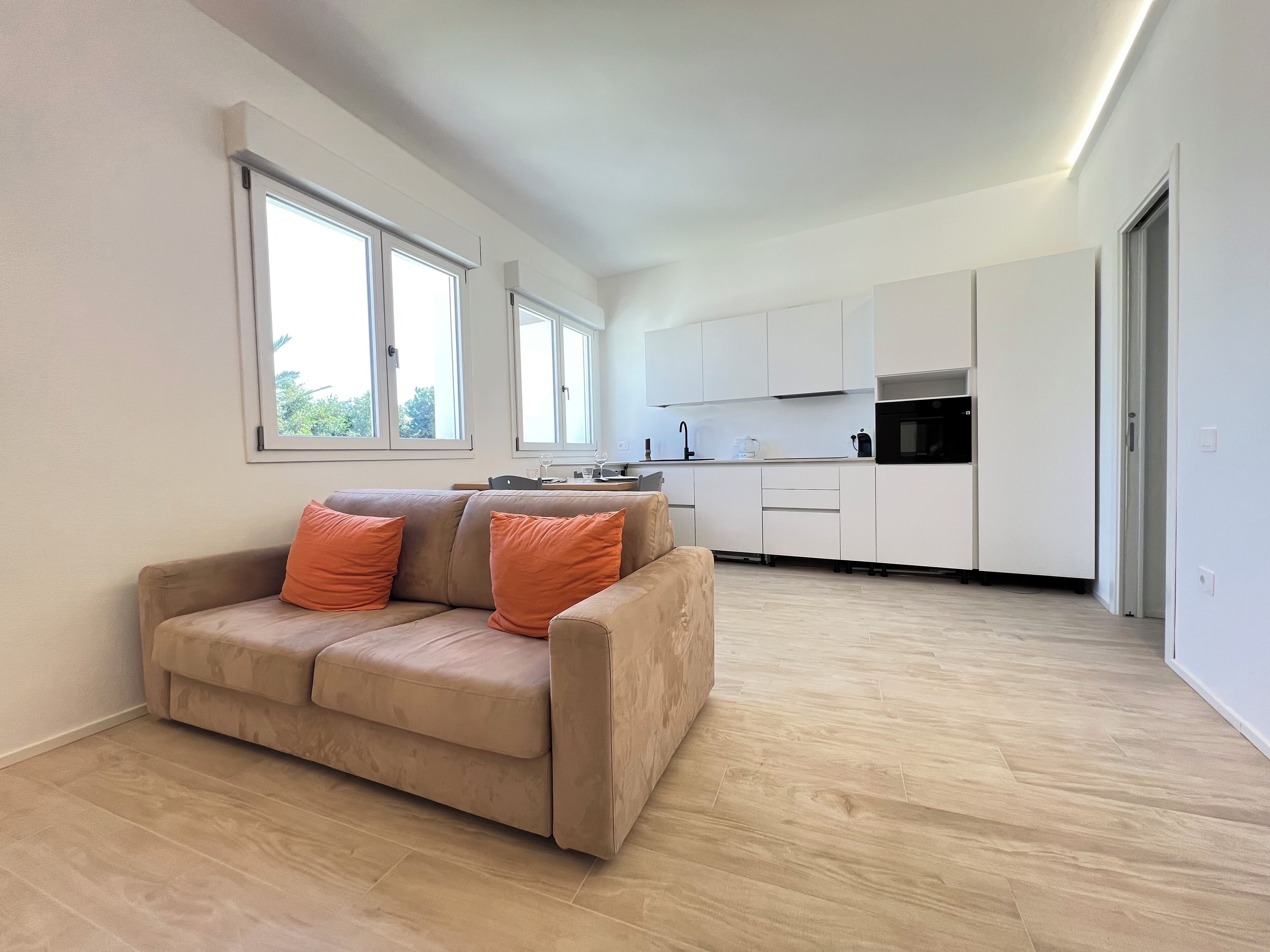 A modern apartment with a sofa, kitchen, and large windows.