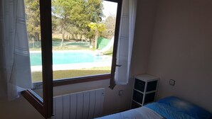 Une chambre avec vue sur une piscine, un lit recouvert d’une couverture bleue et blanche, et un radiateur blanc.
