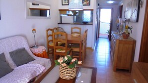 A living room with a sofa, a dining table with chairs, a kitchen area, and a hallway leading to another room. - R. Peñiscola Beach 540 LEK (Peñiscola)