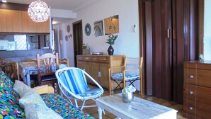 A living room with a colorful sofa, striped armchairs, a wooden coffee table, and a dining area with wooden cabinets and a chair. - R. Peñiscola Beach 540 LEK (Peñiscola)