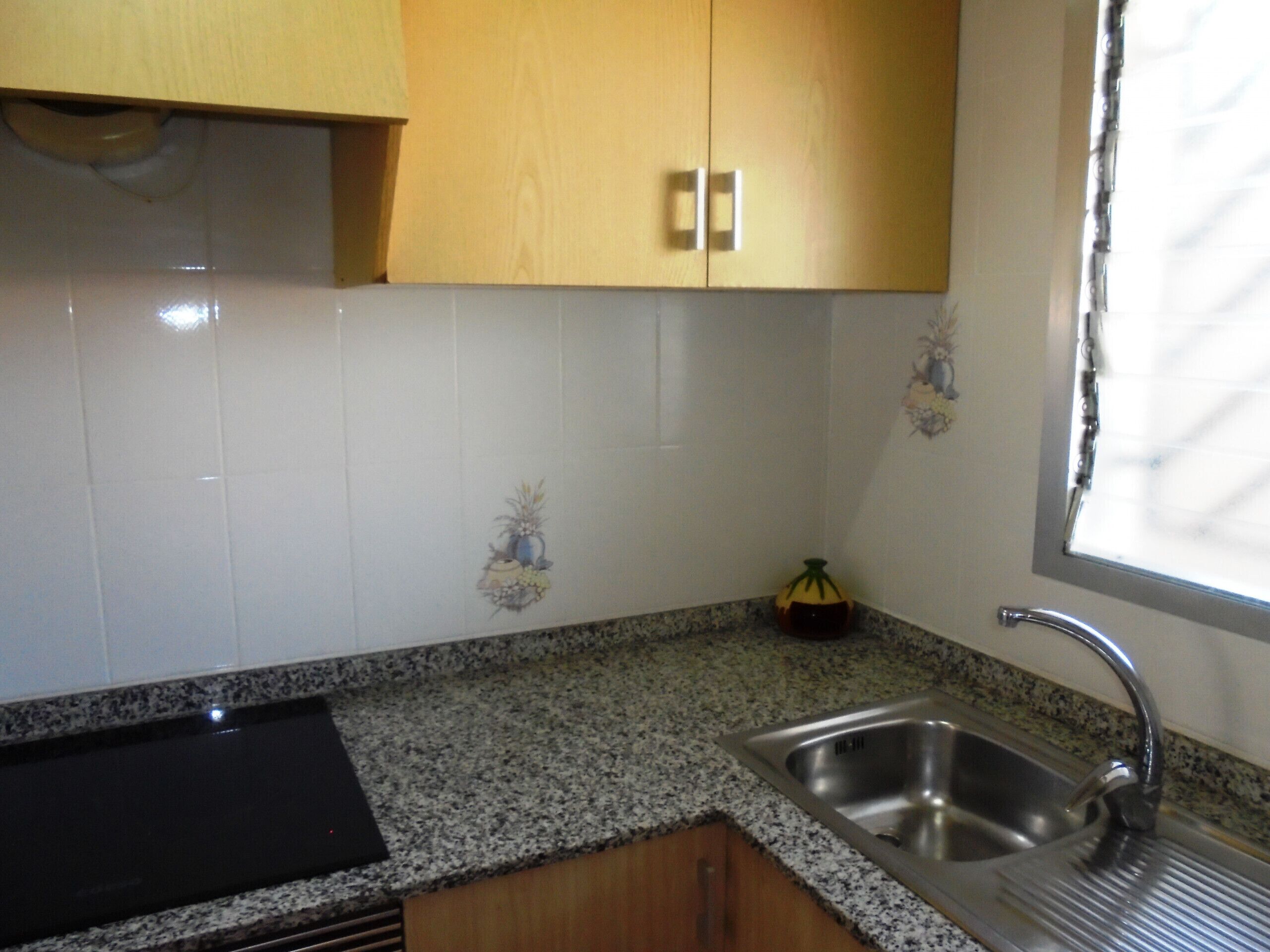 A kitchen with granite countertops, stainless steel sink, wooden cabinets, and decorative tiles.