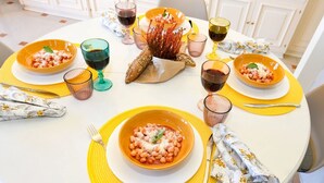 Pyöreä ruokapöytä, jonka päällä on keltaiset aluslautasliinat, useita kulhoja täynnä ruokaa ja viinilaseja.
