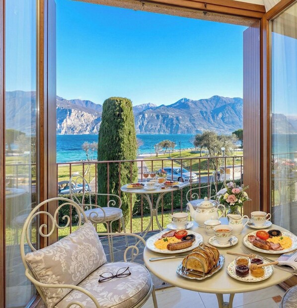 Un balcón con una mesa dispuesta para el desayuno, con vistas a un paisaje montañoso y el mar.