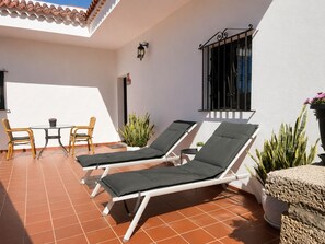 A sunlit patio with two lounge chairs, a small table with chairs, and potted plants.