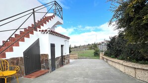 A building with a staircase leading to a gated entrance, a paved area, and a yellow chair.
