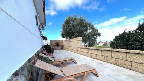 A patio with two wicker lounge chairs, a stone wall, and a view of the surrounding area.