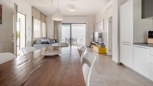 A modern living room with a wooden dining table, white chairs, a sofa, and a TV. - Timeless: Detached Villa with private heated pool and panoramic views (Siracusa)