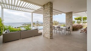 A covered outdoor area with a view of the sea, a seating area, and a dining table. - Timeless: Detached Villa with private heated pool and panoramic views (Siracusa)