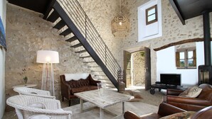 Ein geräumiger Wohnbereich mit Steinwand, Holztreppe, Rattanmöbeln, einem weißen Couchtisch und einem Fernseher.