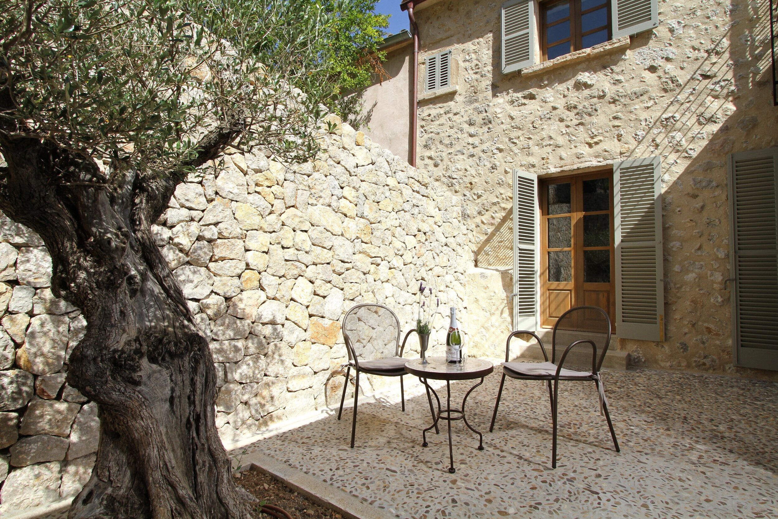 A stone wall, a tree, and a table with chairs in a courtyard.