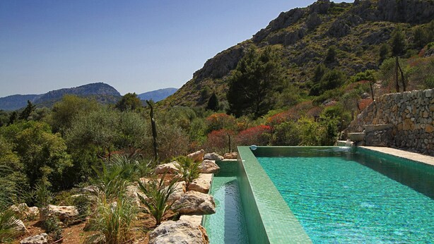 Ein Pool mit klarem, blauem Wasser, umgeben von Felsen und viel Grün, mit Bergen im Hintergrund.
