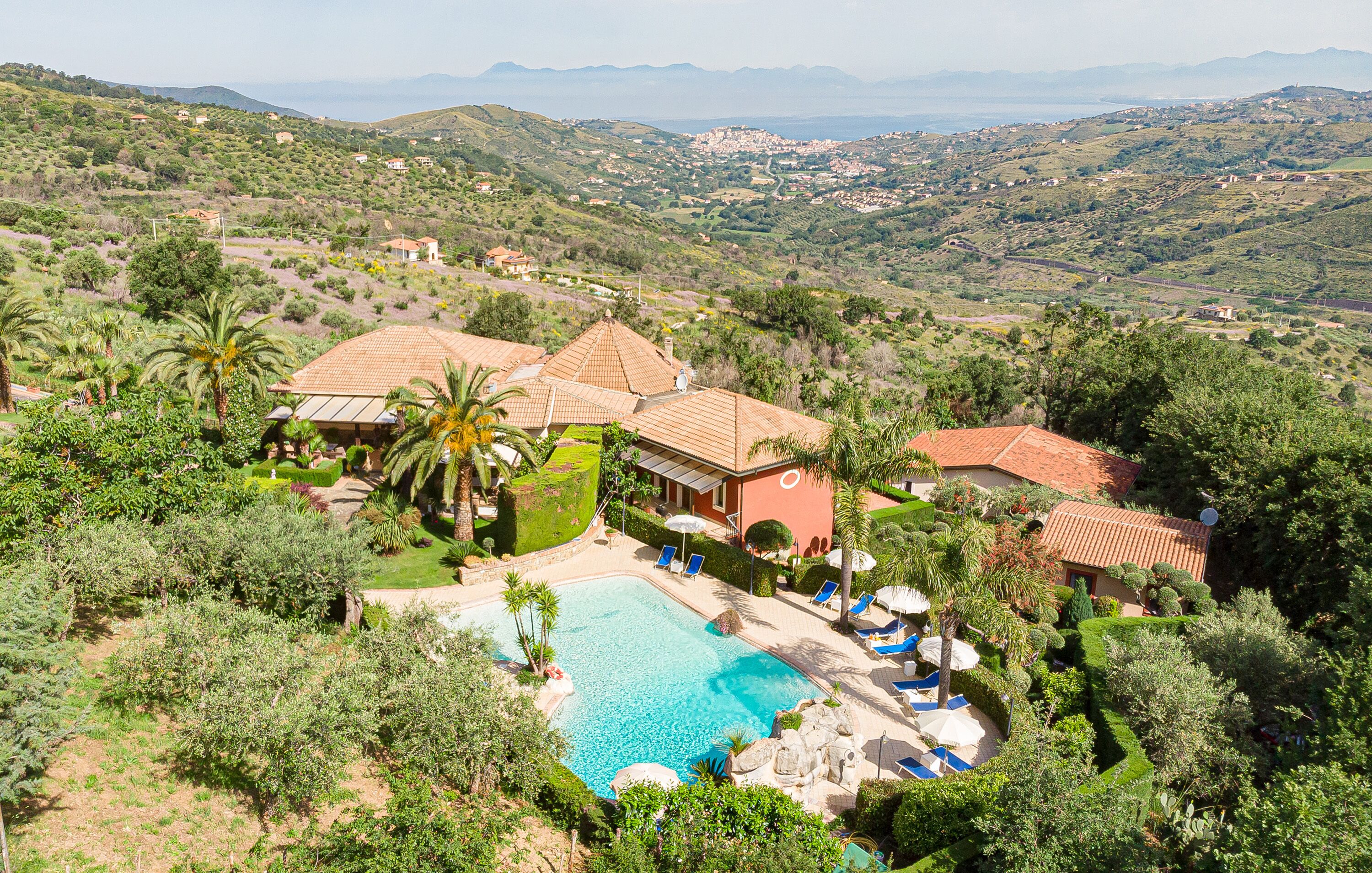 A villa with a swimming pool surrounded by lush greenery and hills.