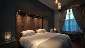 A modern bedroom with a large bed, a stone accent wall, and a window with curtains. - Apartment in Prestigious location Central Edinburgh  (Edinburgh)