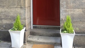 A red door with a brass plate, two white planters with green plants, and a doormat on a stone-paved entrance. - Apartment in Prestigious location Central Edinburgh  (Edinburgh)