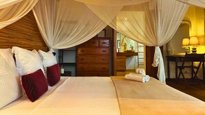 Un dormitorio con cama a dosel, cabecera de madera, un tocador y un escritorio con lámpara.