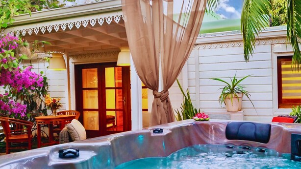 Un jacuzzi con toldo color beige, rodeado de mobiliario exterior y plantas en macetas.