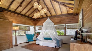 Una habitación con techo de madera, una cama con dosel, una silla azul y un escritorio con computadora.