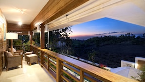 Un balcón con mobiliario de mimbre y vista a un paisaje al atardecer.