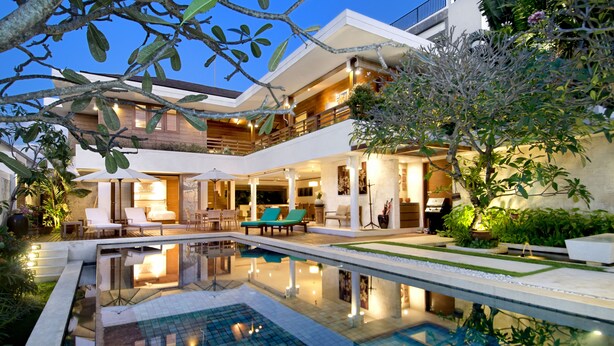 Una casa moderna con piscina, mobiliario exterior y una zona de patio bien iluminada.