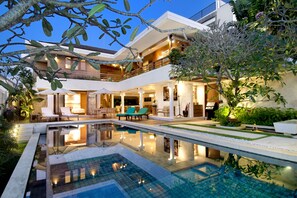 Una casa moderna con piscina, mobiliario exterior y una zona de patio bien iluminada.