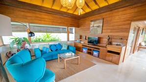 Una sala de estar moderna con un sofá azul, una mesa de centro y un televisor. Se observan armarios de madera y un ventanal con plantas.