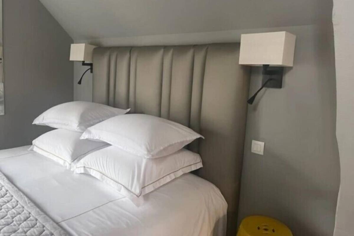 A neatly made bed with white linens and pillows, a headboard with vertical lines, and two wall-mounted light fixtures on either side.