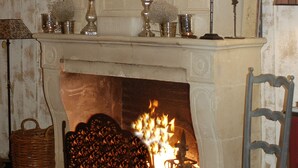 A fireplace with a fire, a mantel with decorative items, and a chair. - La Demeure de l'Ile (Craon)