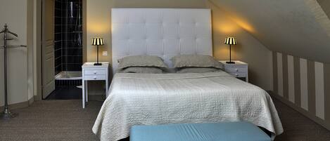 A bedroom with a large bed, two bedside tables, a bench, and a door leading to a bathroom.