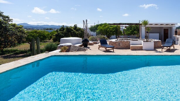 Una piscina con sillones de descanso y una pérgola, rodeada por un jardín y vistas a las montañas.