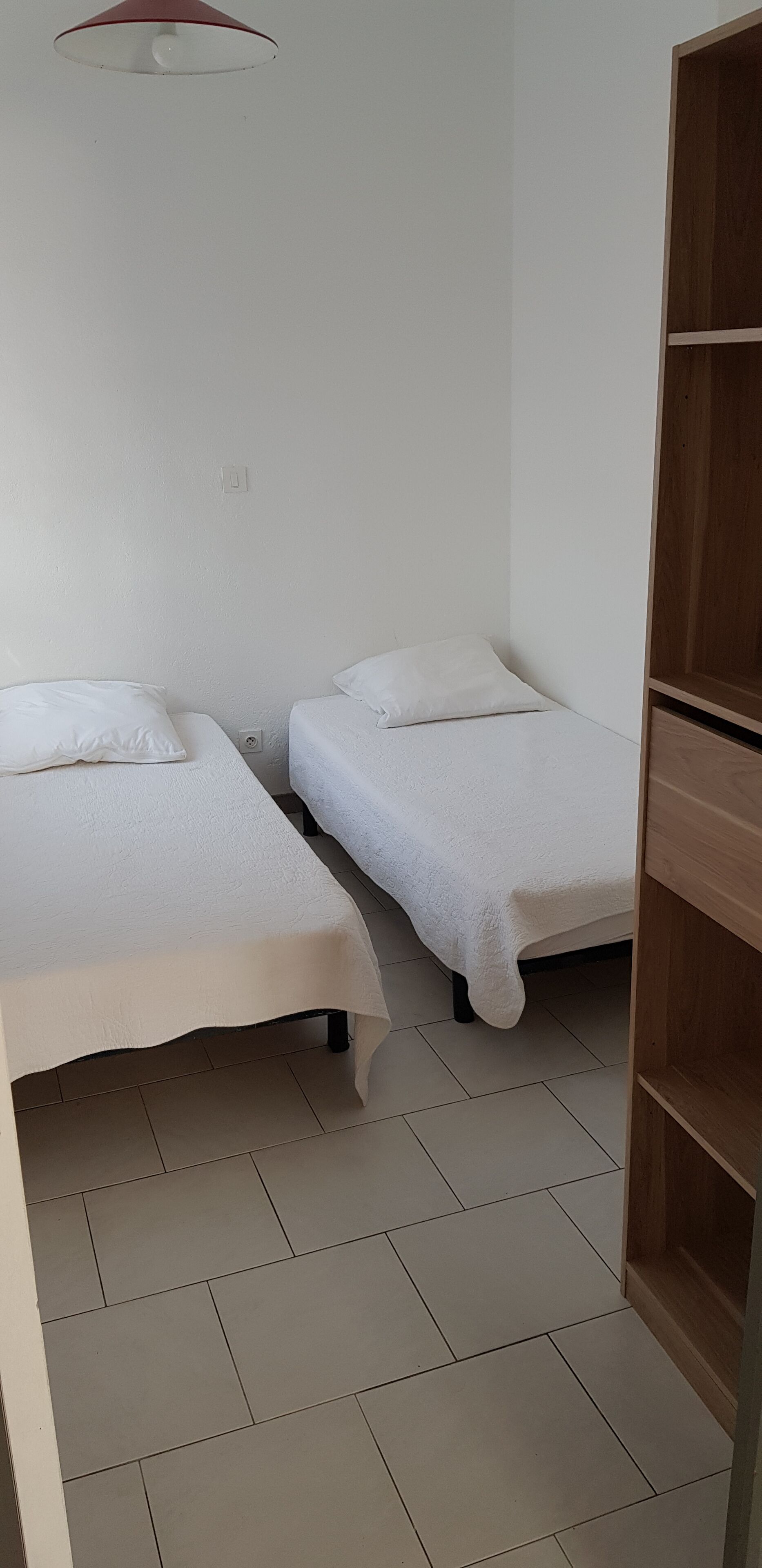 Ein Zimmer mit zwei Einzelbetten, einem Holzschrank und einem Fliesenboden.