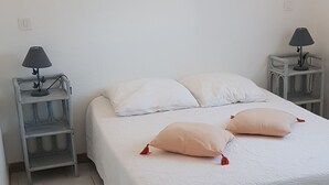 A neatly made bed with white bedding and two decorative pillows, flanked by two bedside tables with lamps. - Small house 4/6 persons 700 m from the beach of st cyprien (Porto-Vecchio)