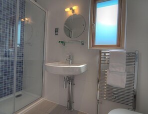 Een badkamer met een douchecabine van glas, een wit wastafelmeubel, een spiegel en een handdoekrek.